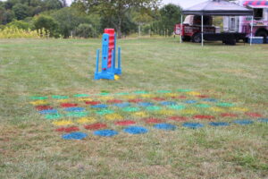 Colorful chalk-like patterns on the grass with a blue and red plastic game near a food-truck tent in the background.